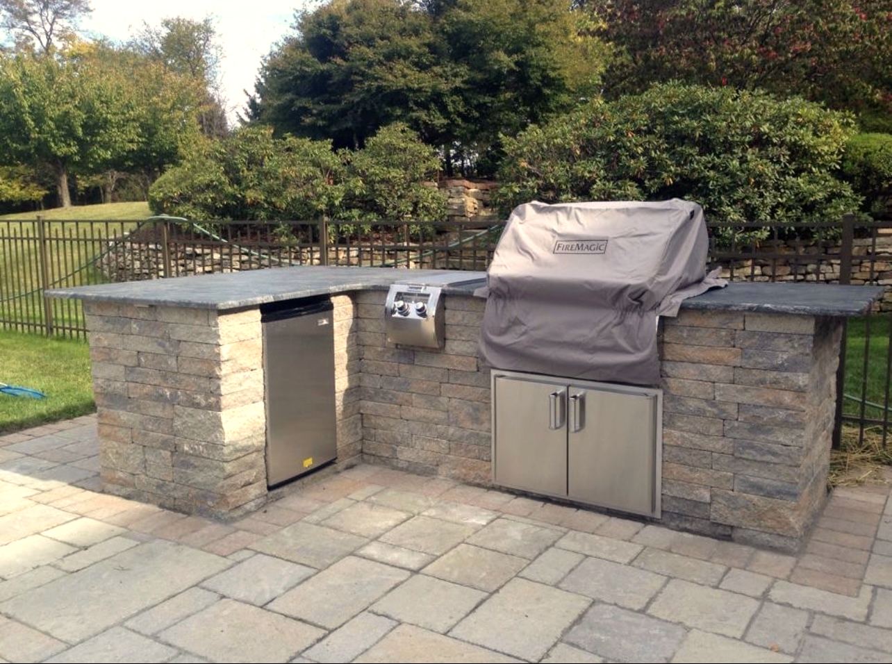 Built-in outdoor kitchen in natural stone with grill and refrigerator