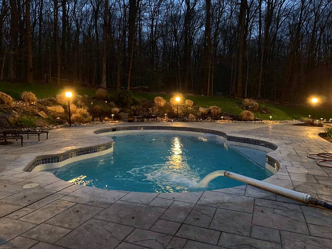 Pool at dusk with landscape lighting around the patio, new tile and plaster