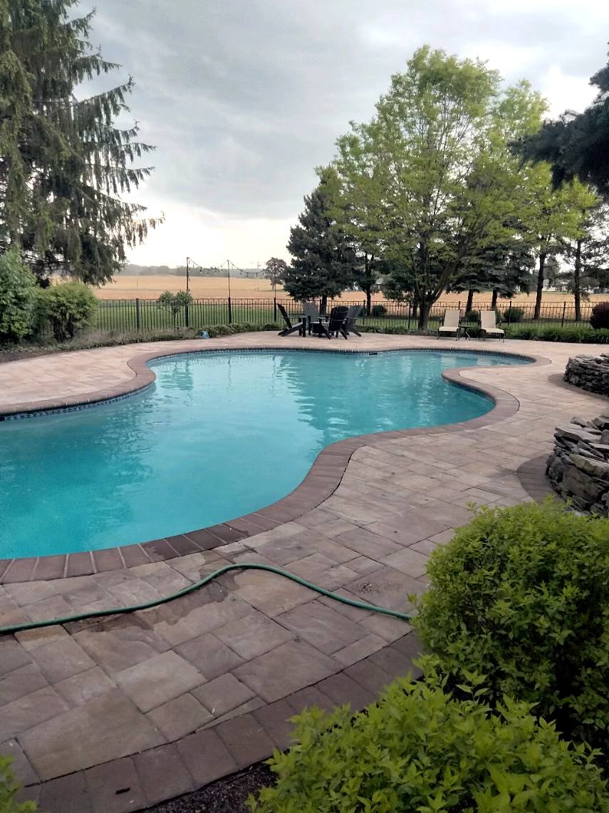 Freeform pool with brick coping and paver deck looking out over farm fields