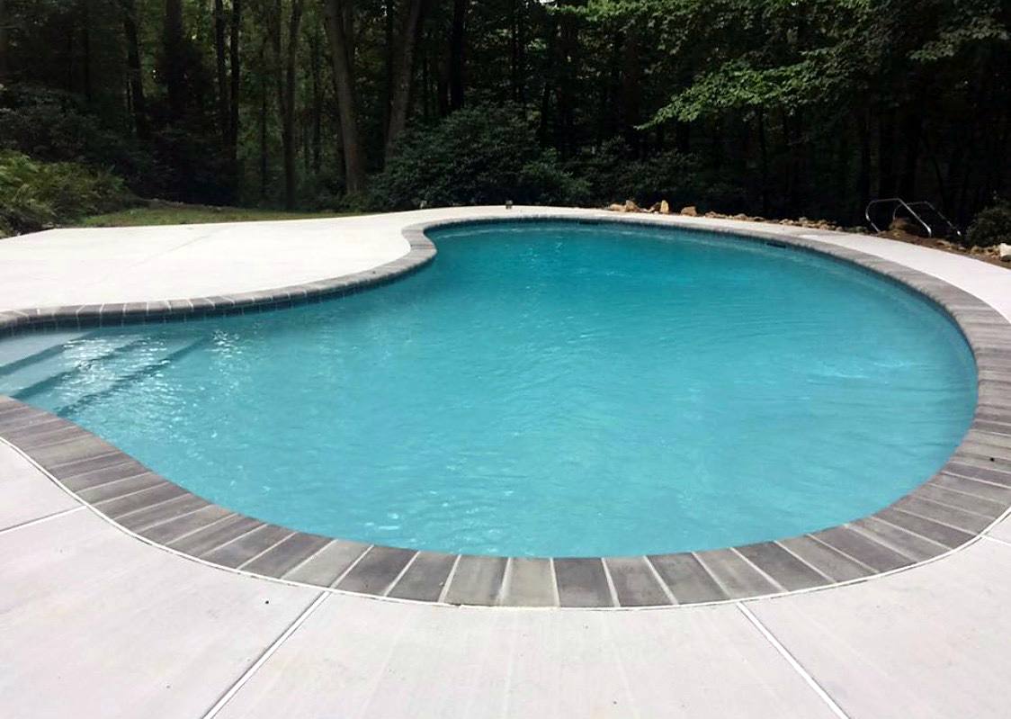 Freeform pool with new plaster, brown coping and a broom-finished concrete deck