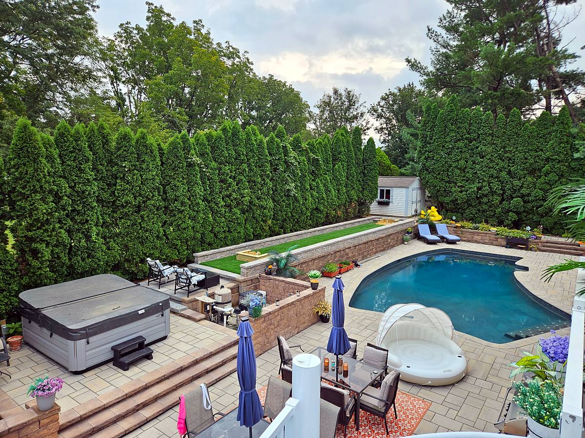 Overhead view of a whole-yard renovation: paver patios on two levels, a hot tub, a walled turf horseshoe pit and the pool