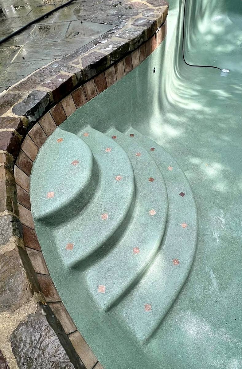 Curved pool steps in a Jade mini pebble finish, seen through the water, with stone coping