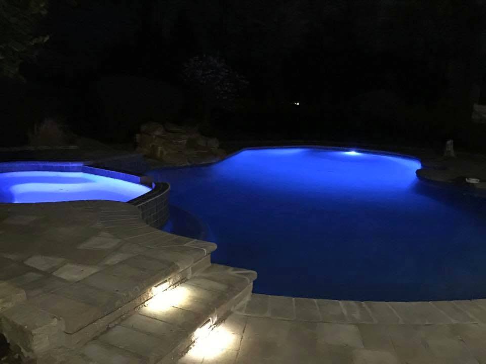 Pool and spa lit blue at night, with step lights on the patio