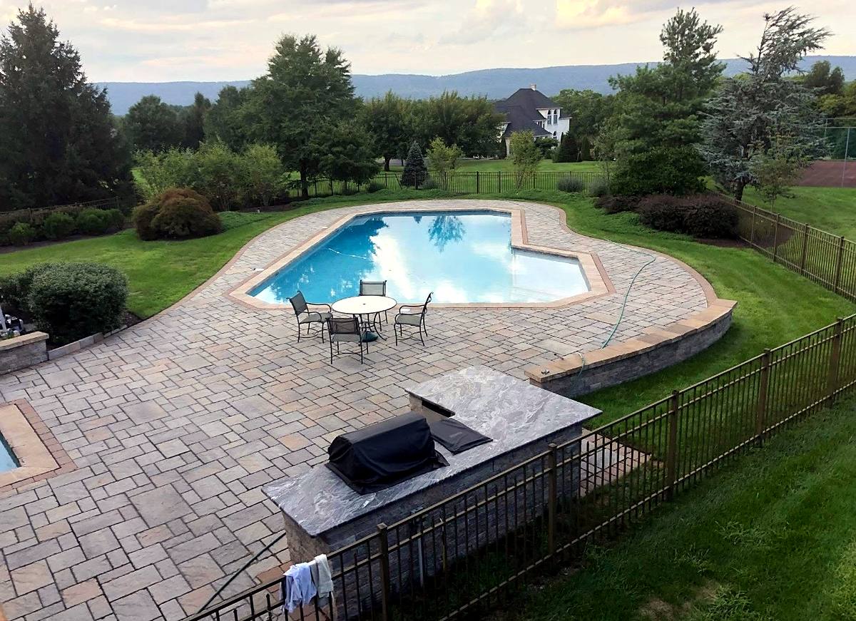 Overhead view of a pool, paver deck, sitting wall and granite-topped outdoor kitchen with hills behind