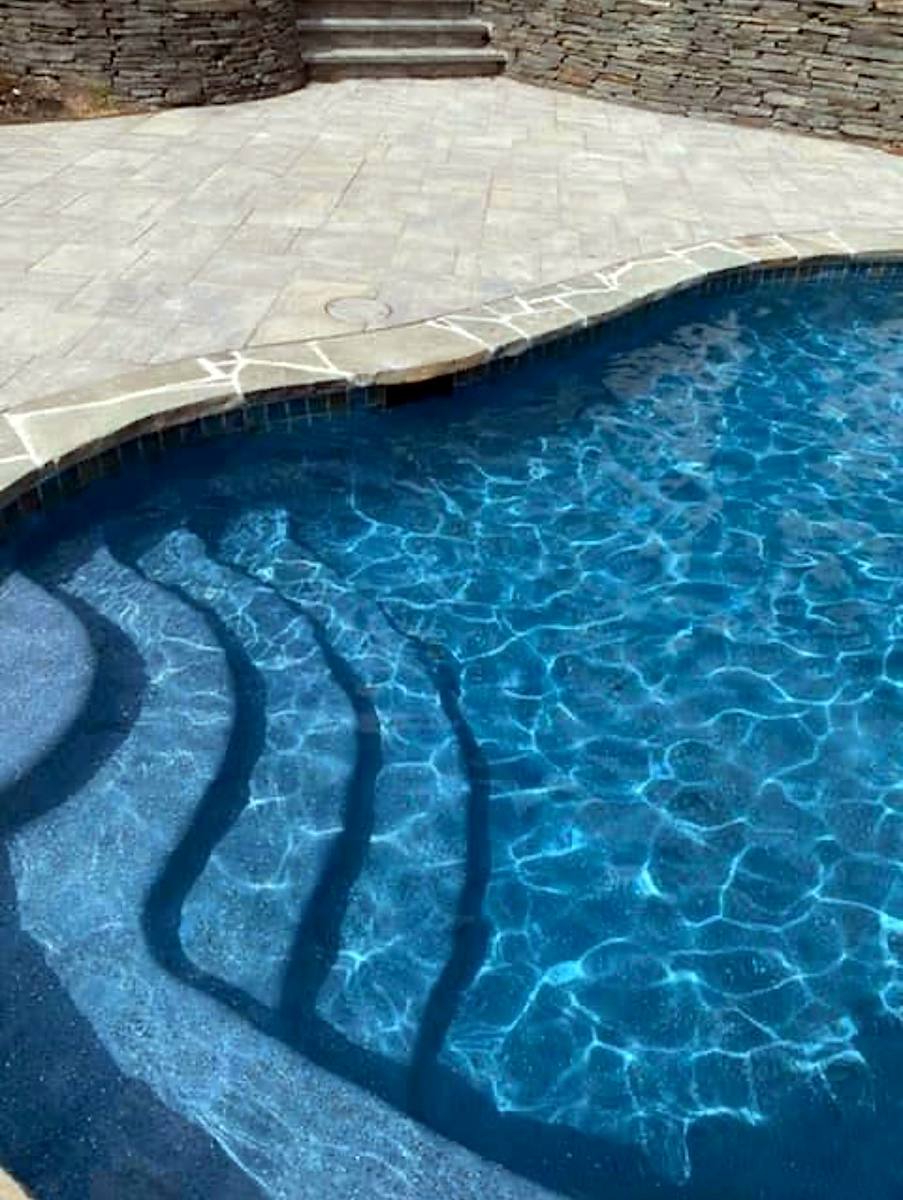 Curved pool steps in a blue pebble finish with flagstone coping and paver deck