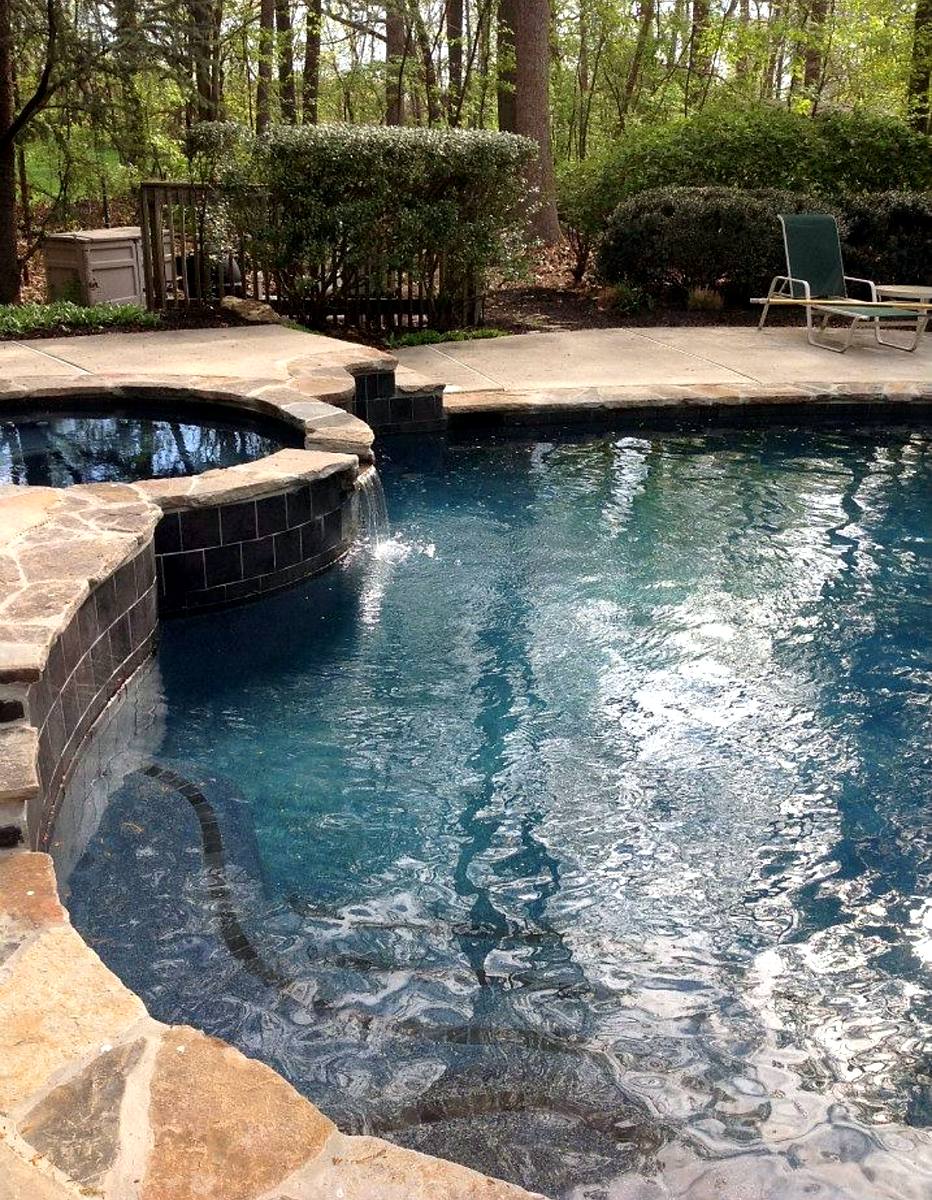 Raised spa in natural rock spilling over dark tile into the pool