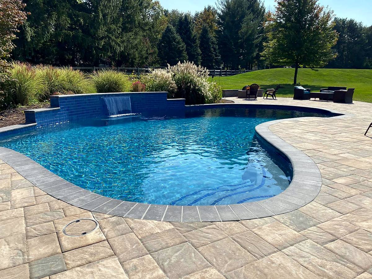 Freeform pool with a raised blue-tile wall and sheer descent waterfall, new paver deck
