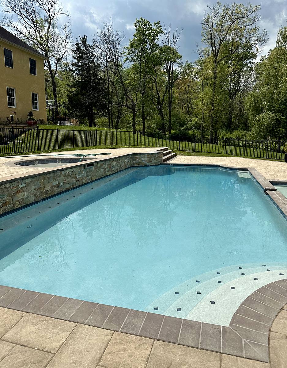 Freshly filled pool with a raised stacked-stone spa wall, new coping and paver deck