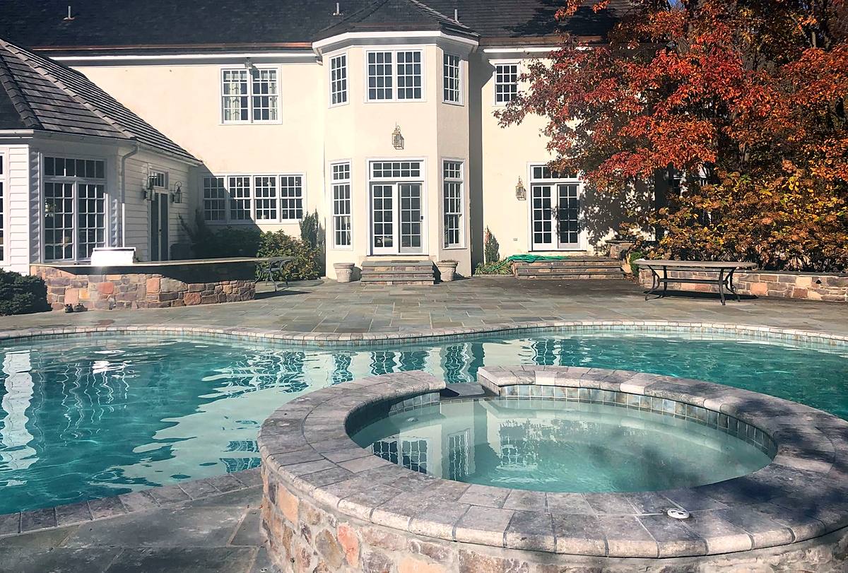 Pool and raised stone spa behind a stucco house in autumn