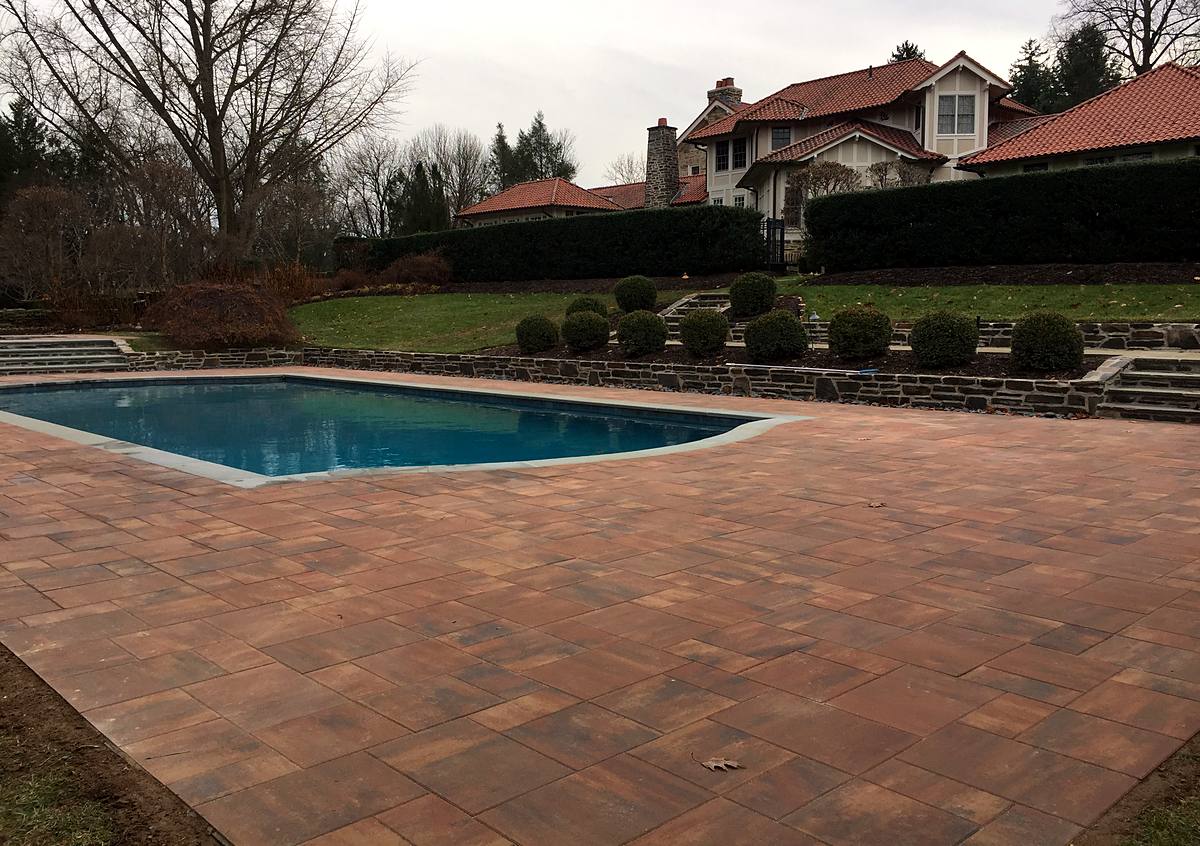 Rectangular pool with new plaster and a terracotta paver deck below a tile-roofed house