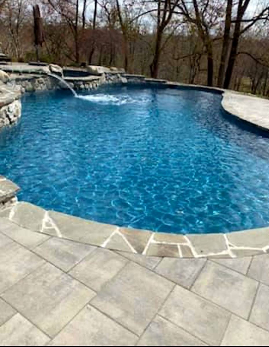 Freeform pool with a natural stone waterfall, flagstone coping and paver deck