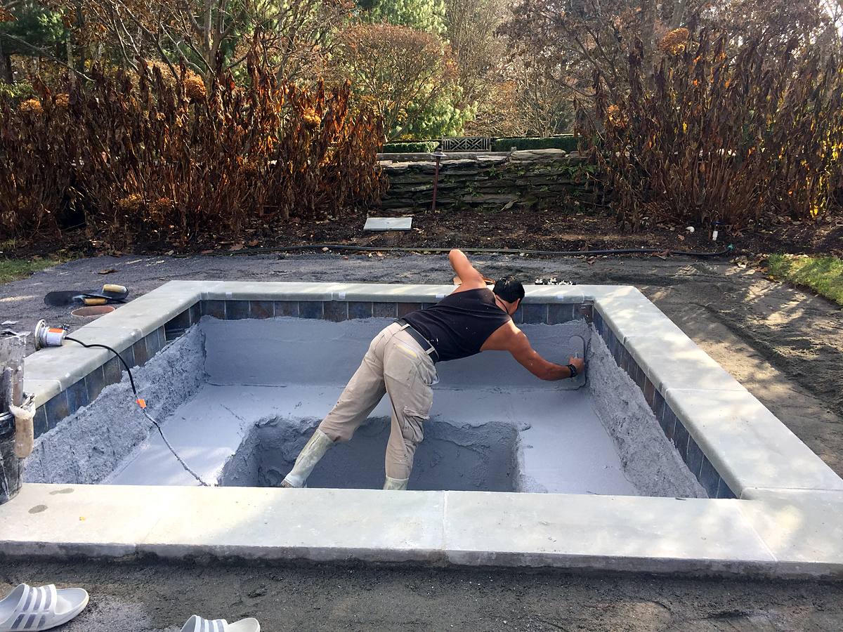 Crew troweling grey bond coat onto a pool shell with the new waterline tile already set