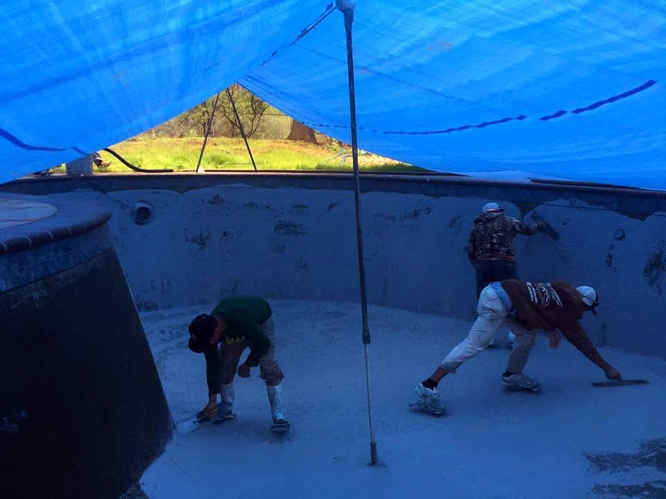 Crew hydroblasting old plaster from a pool under a tarp